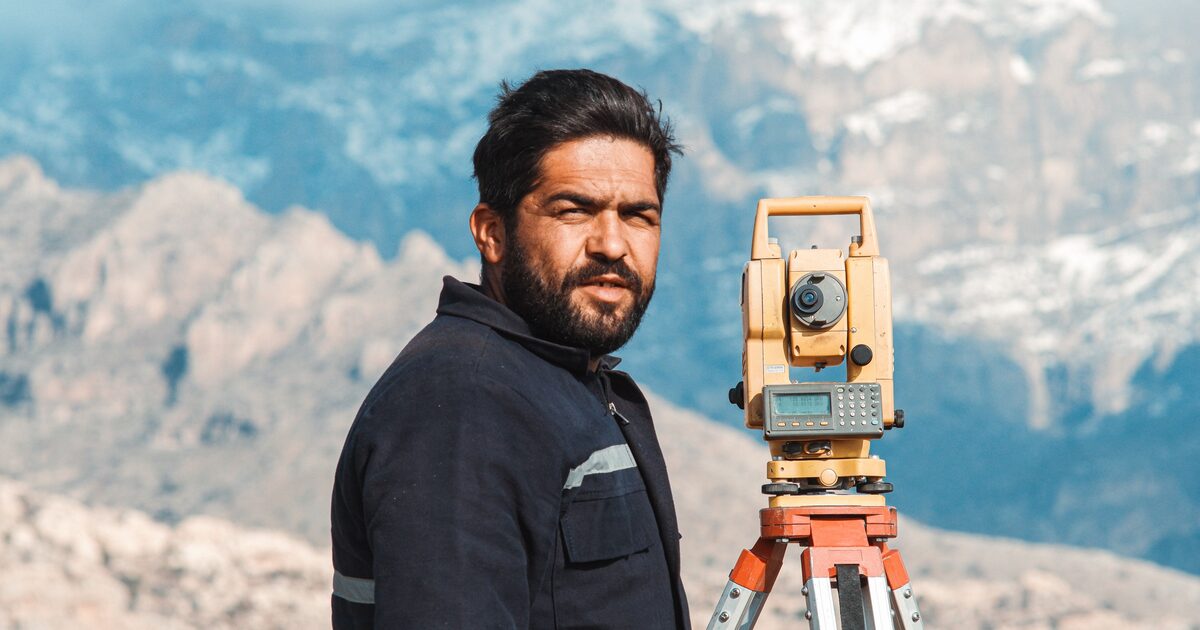 A surveyor standing in mountainous terrain with measuring equipment, checking the real scope of the ground against the plan
