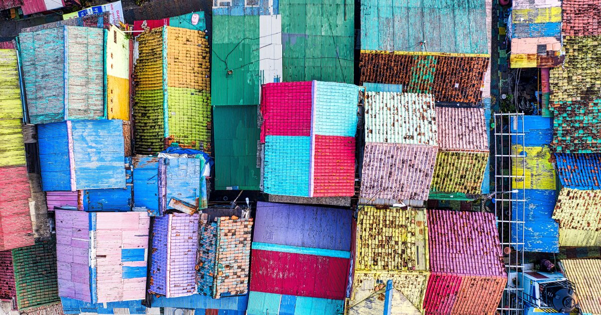 Aerial view of uniquely colored rooftops packed together, each roof a different place rather than a copy of the last